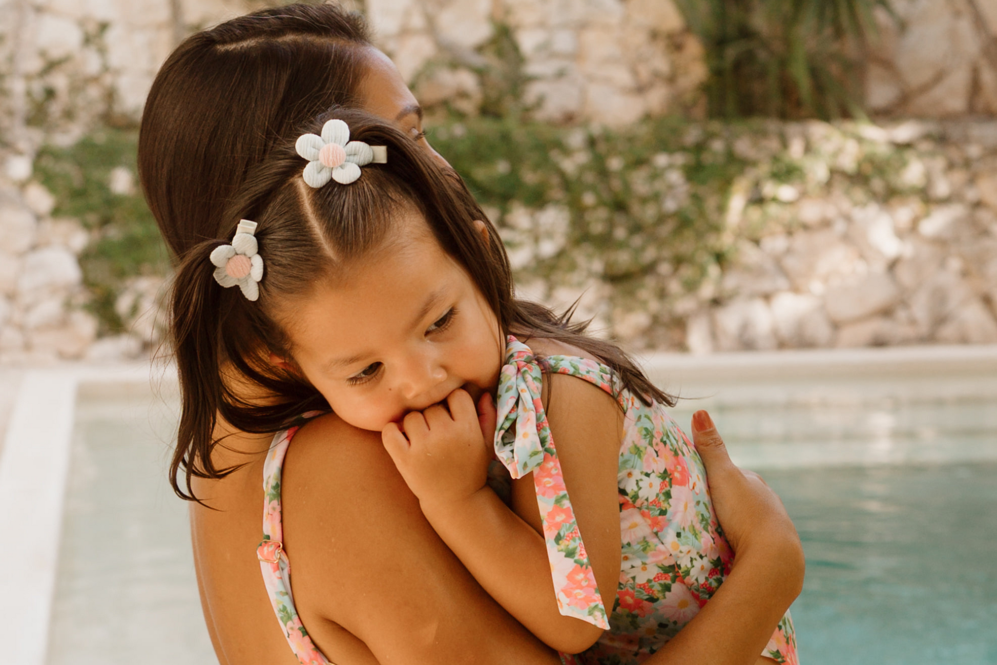 Woman holding a child in matching floral swimsuits by a pool.