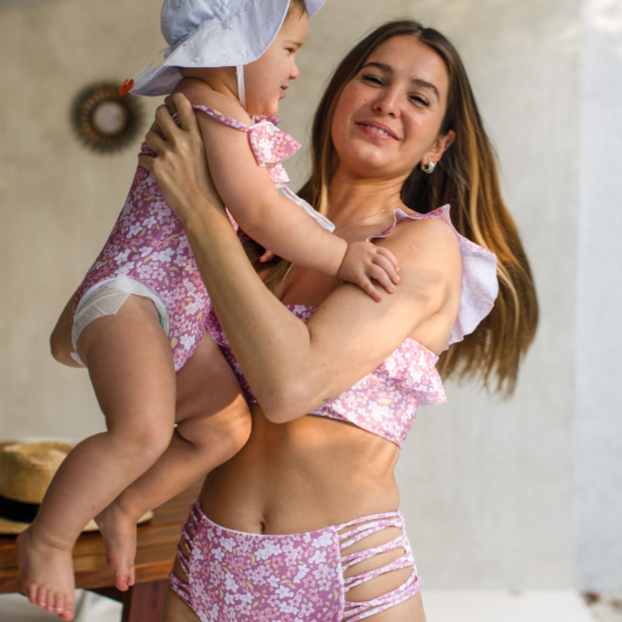 Woman and child in matching pink swimsuits standing close together outdoors.