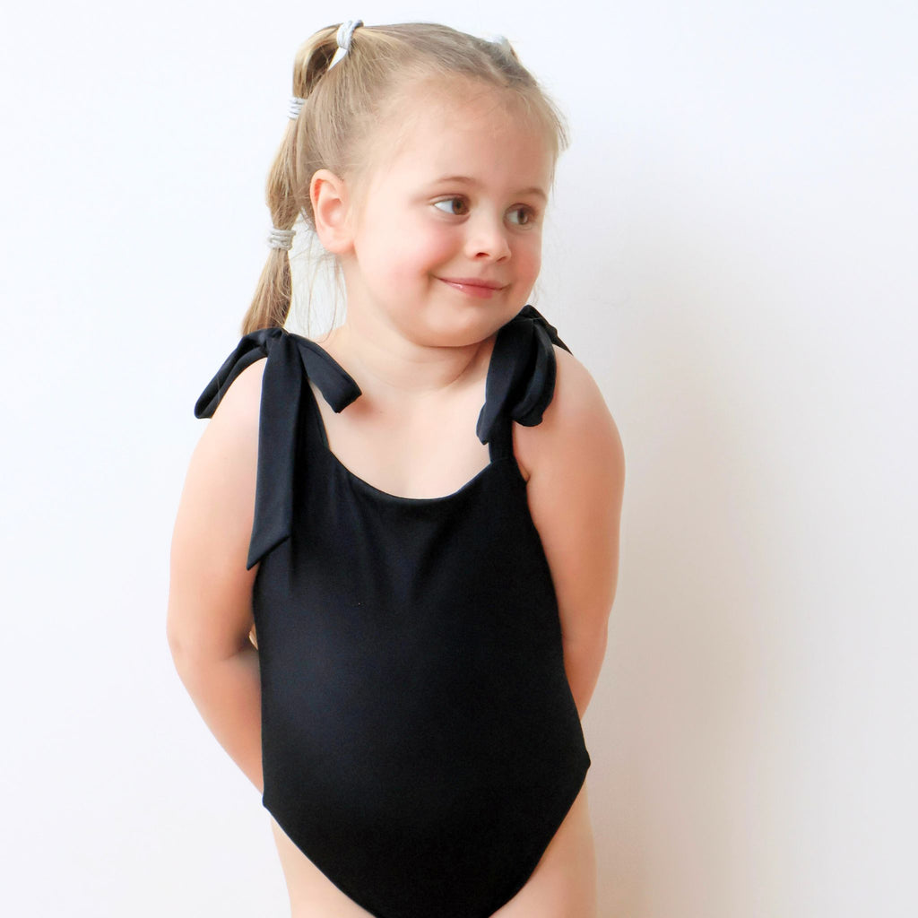 Black one-piece swimsuit for kids, front view with bowknot straps